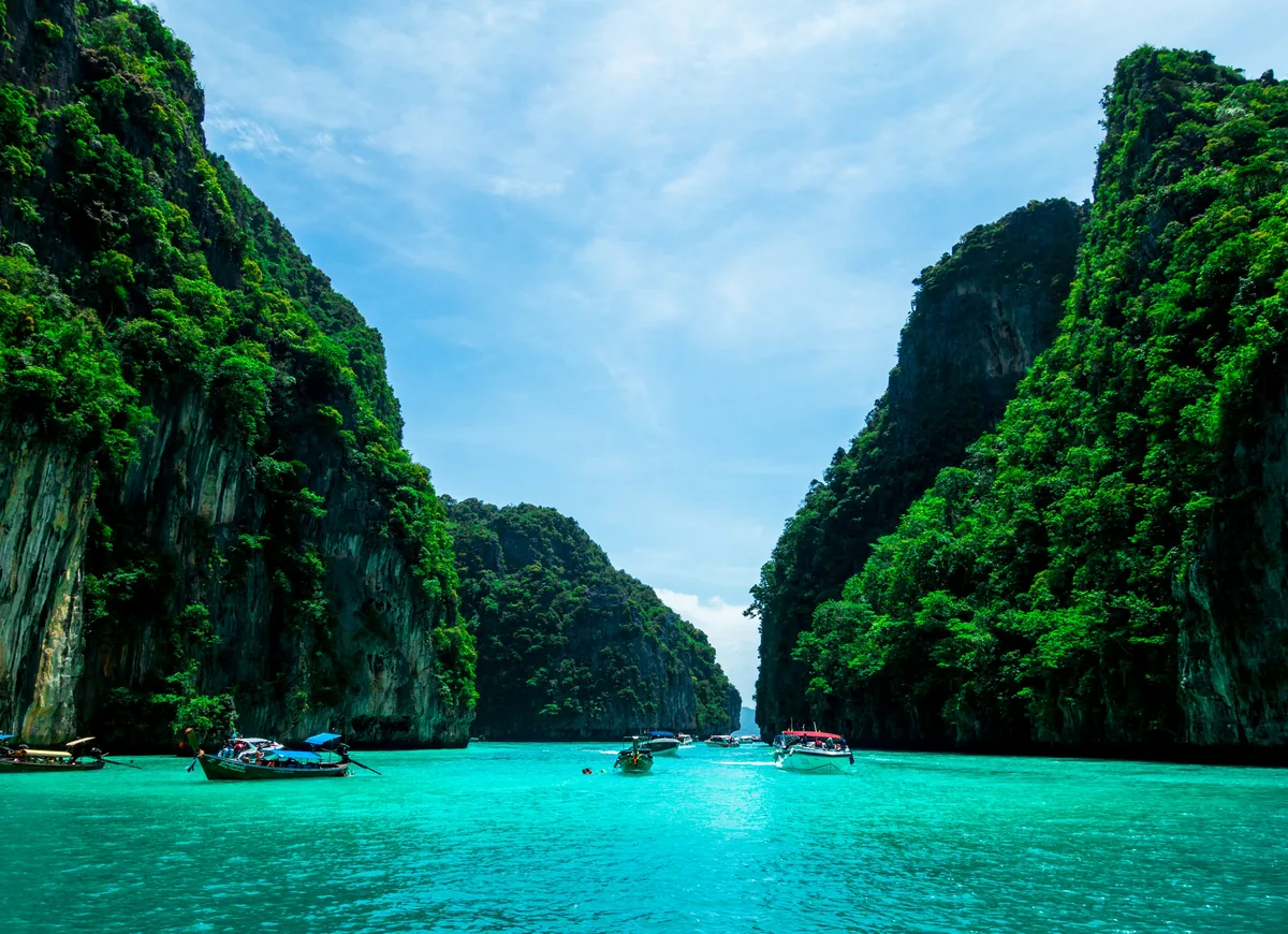 Turquoise lagune tussen begroeide kalksteenrotsen bij Phuket, met longtailboten.