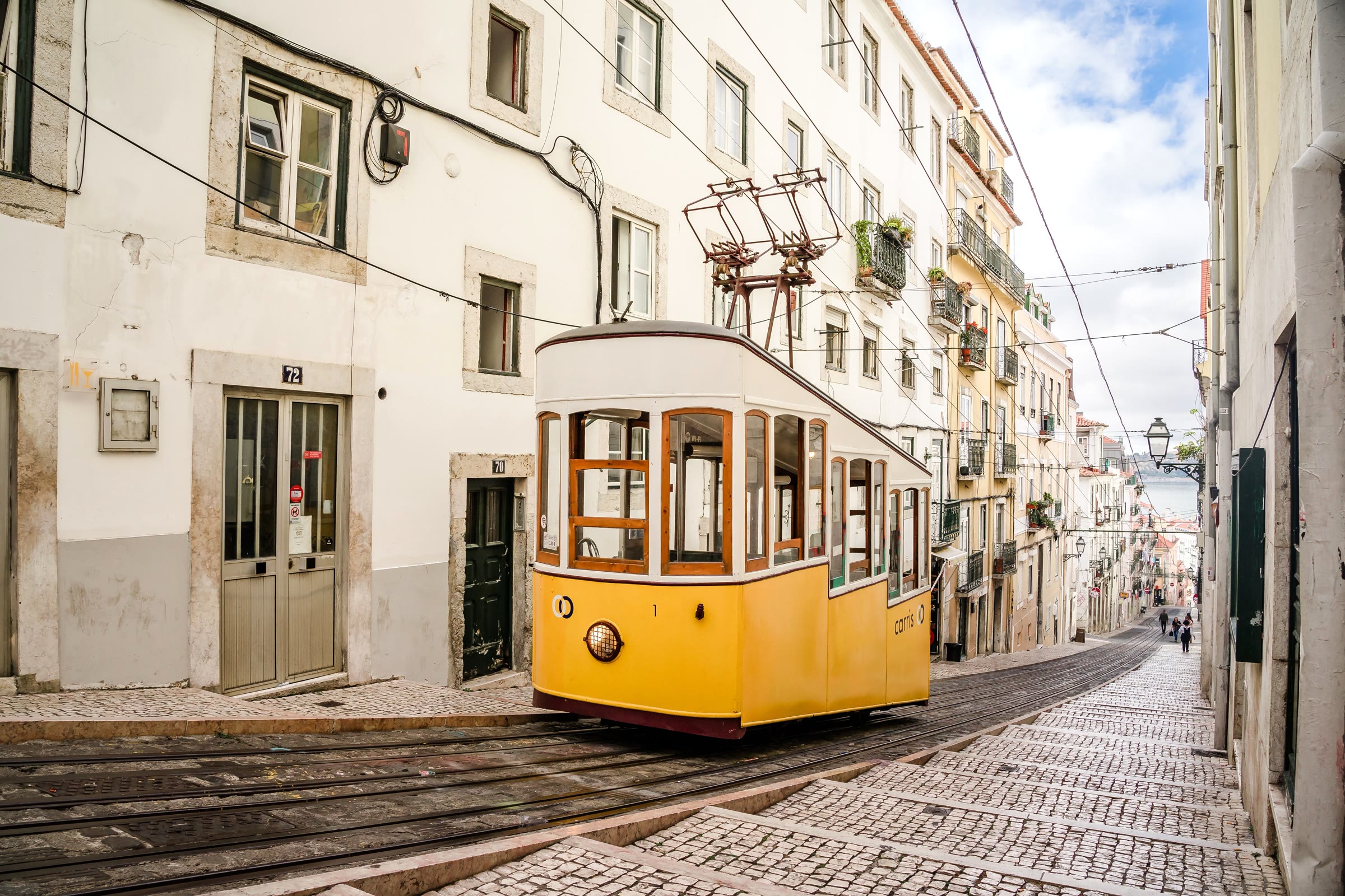Gele kabeltram op de kasseien van een steile straat tussen herenhuizen in Lissabon.