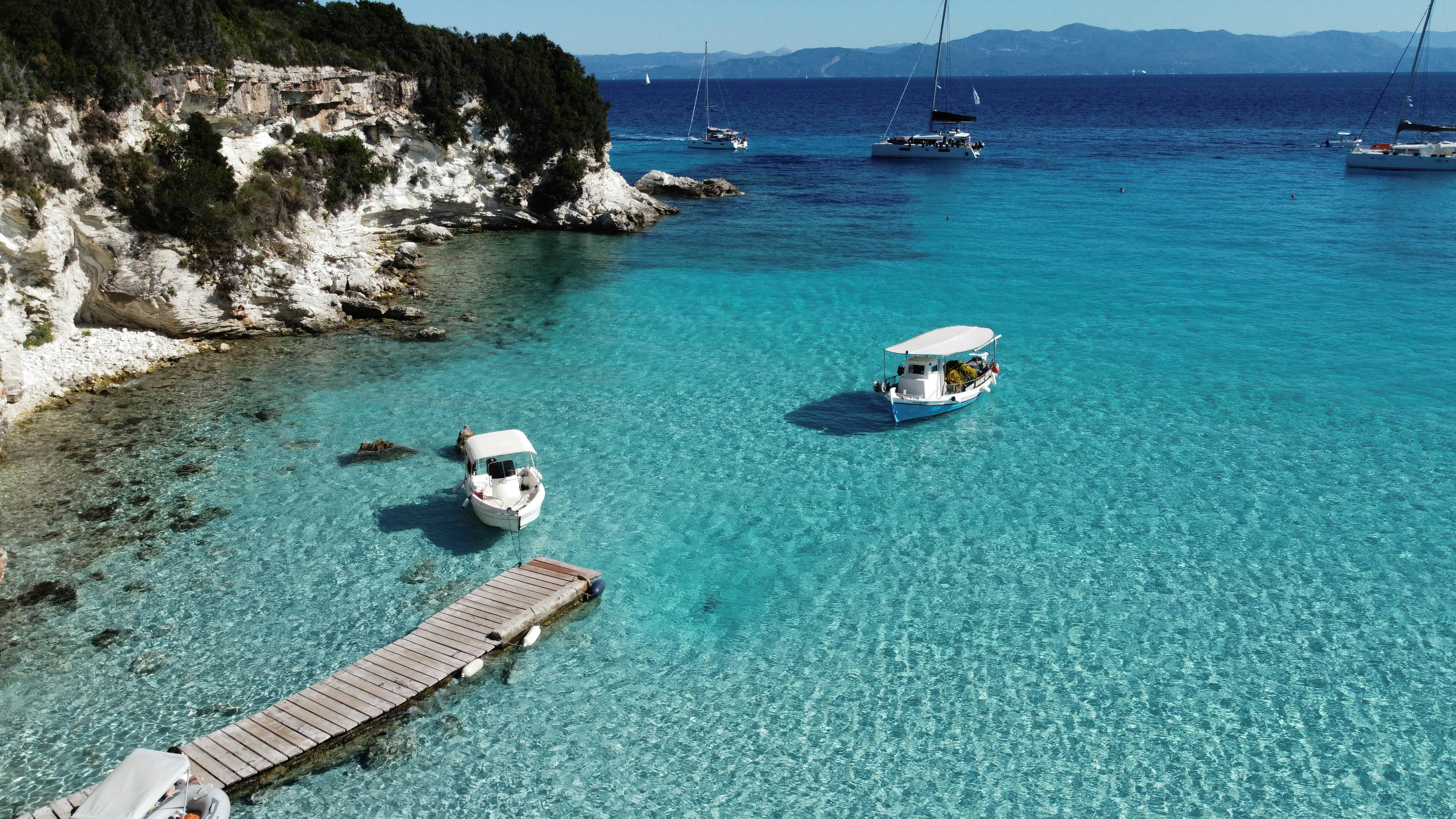 Groene kustklif boven een heldere turquoise baai met boten en een houten steiger