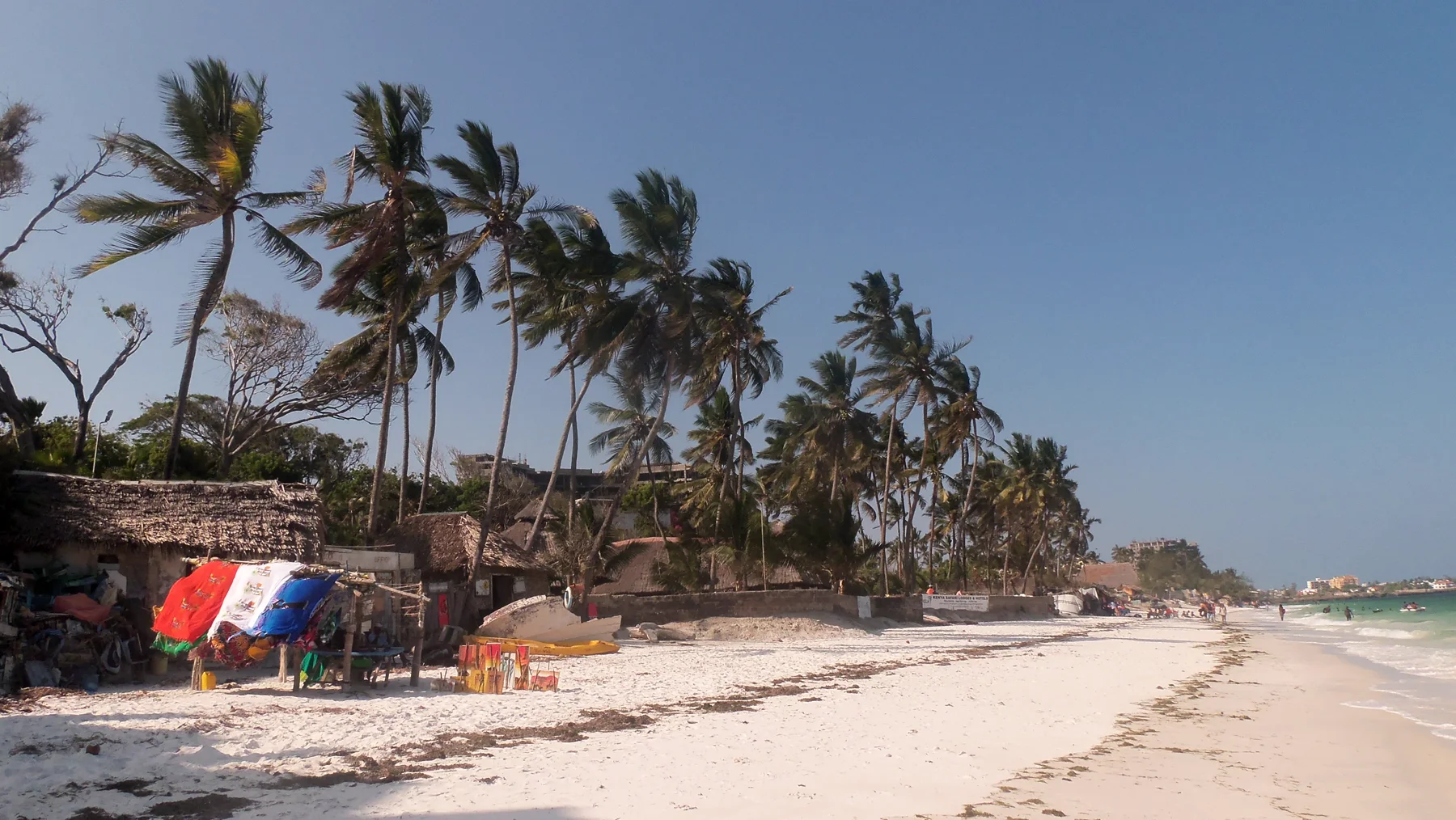 Palmbomen en strandhutten langs het witte zandstrand van Mombasa, met de Indische Oceaan op de achtergrond