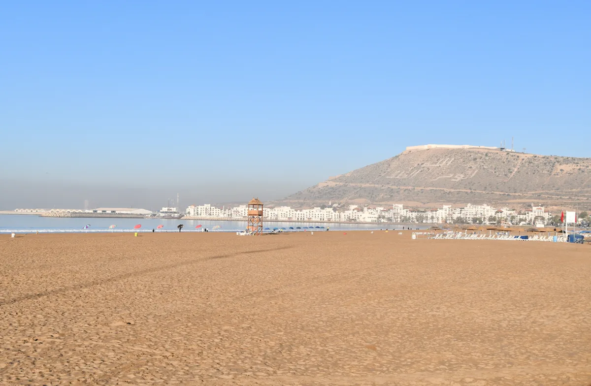 Kamelen en een paard op het strand van Agadir met golven en zwemmers aan de Atlantische kust