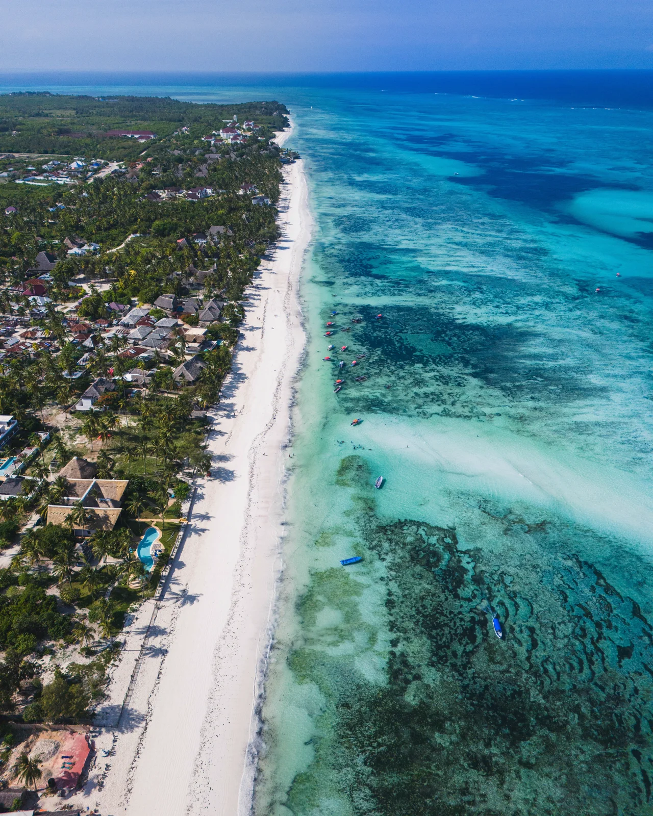 Luchtfoto van de kustlijn van Zanzibar, met een wit strand tussen groen landschap en turquoise zee met koraalriffen