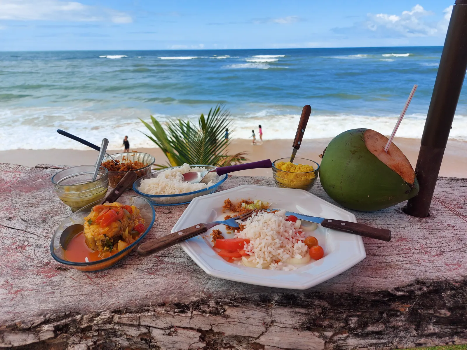 Hangmat en houten picknicktafels tussen palmbomen op een wit strand, met zee op de achtergrond